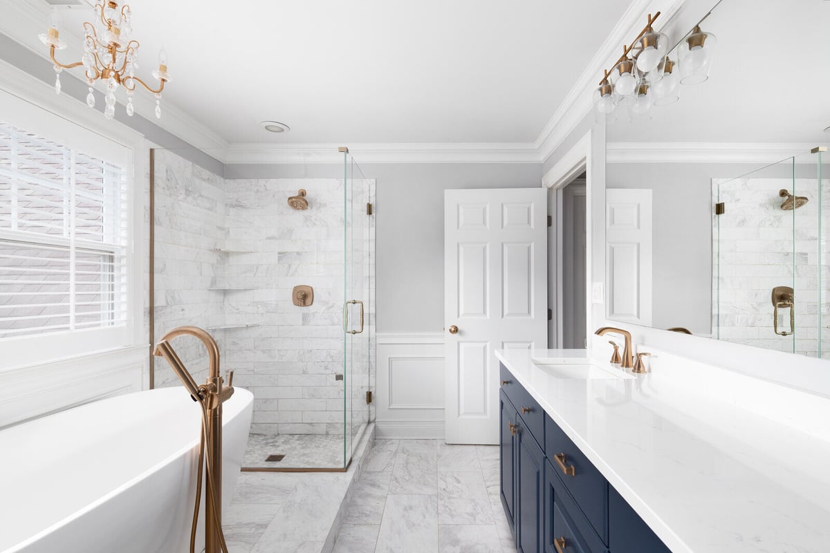 Luxurious white marble bathroom remodel with navy blue vanity and gold fixtures by Triple Crown Contractors in Apex, NC