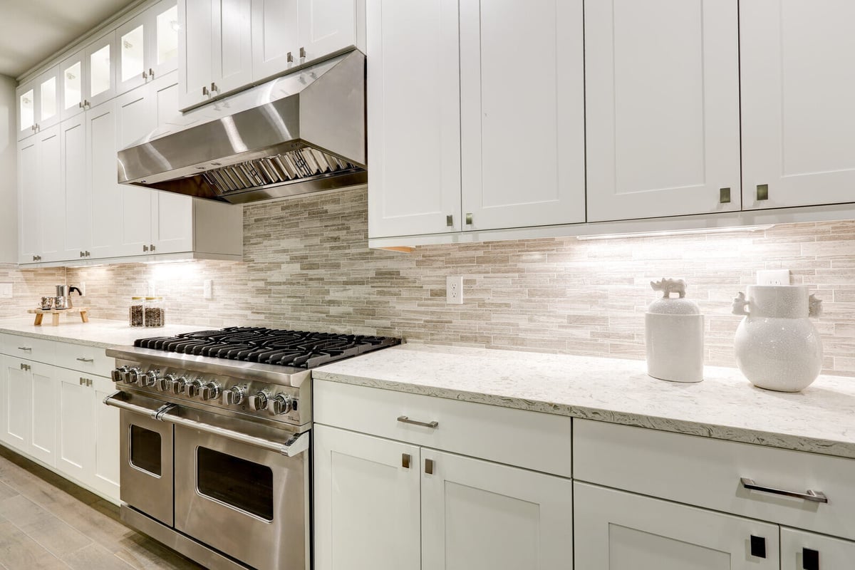 Modern kitchen featuring a stainless steel range hood, bright white cabinets, and sleek under-cabinet lighting in Durham, NC