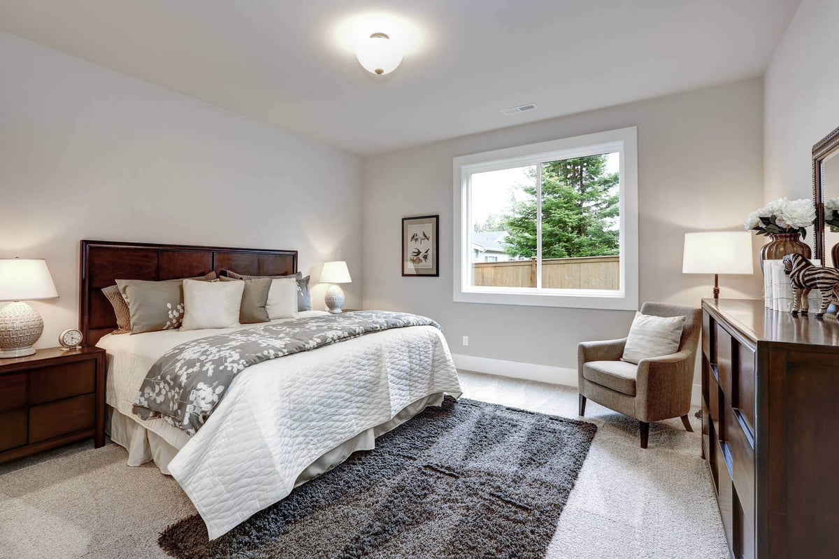 Modern master bedroom featuring soft lighting, plush carpeting, and a large window, designed by Triple Crown Contractors in Durham, NC